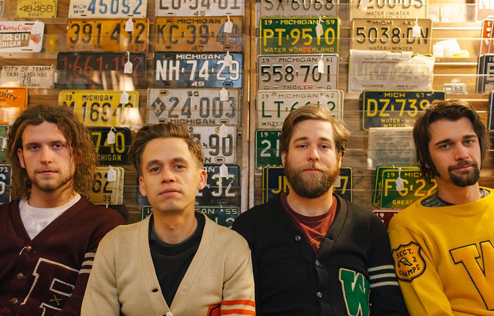 The four members of The Go Rounds sitting in front of a wall of Michigan license plates
