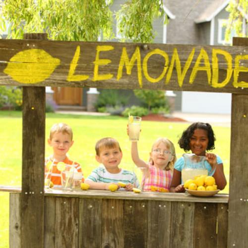 Four kids working at a lemonade stand in the front yard of a house
