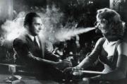 A woman blows smoke at a man in an old timey bar