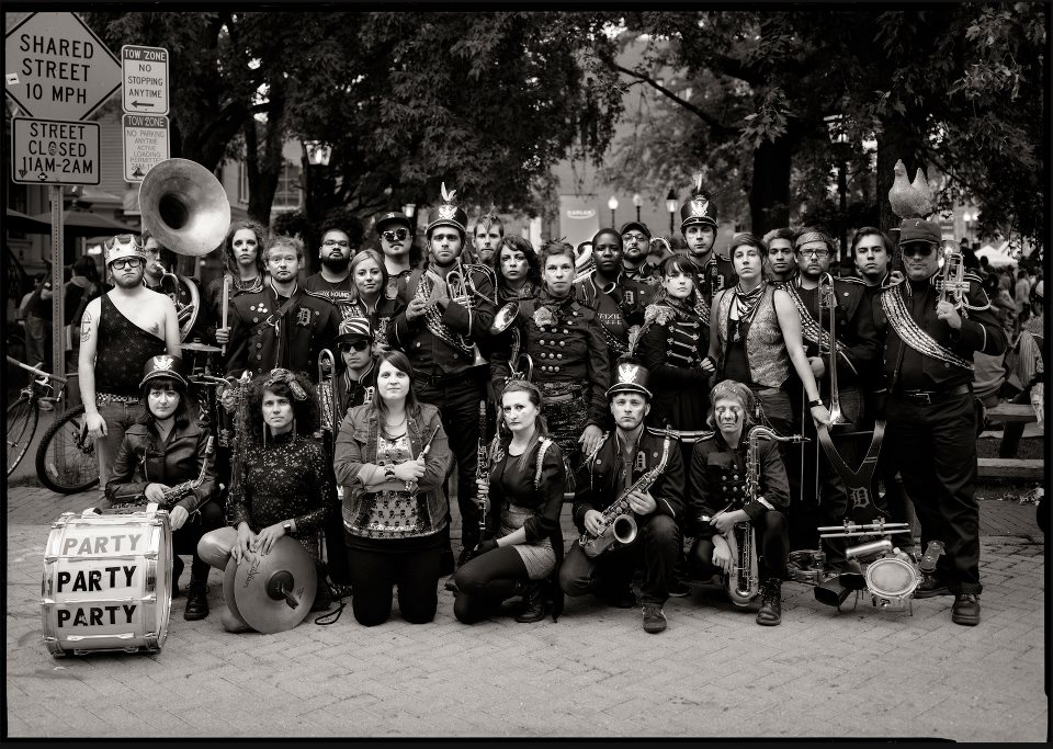 Large group of musicians in eclectic marching band costumes posing in the street