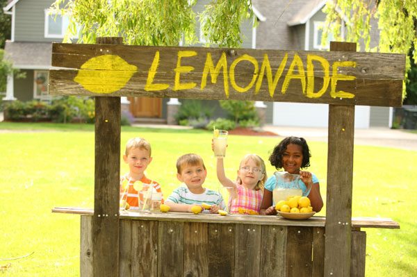 Four kids working at a lemonade stand in the front yard of a house
