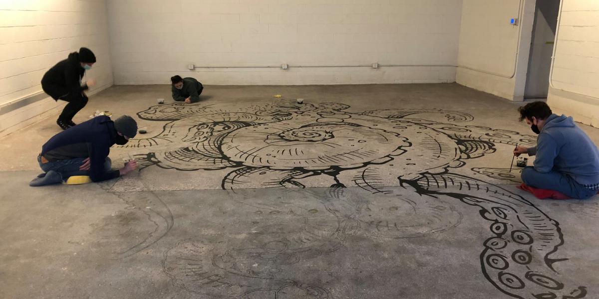 Group of volunteers painting an octopus mural on the concrete floor