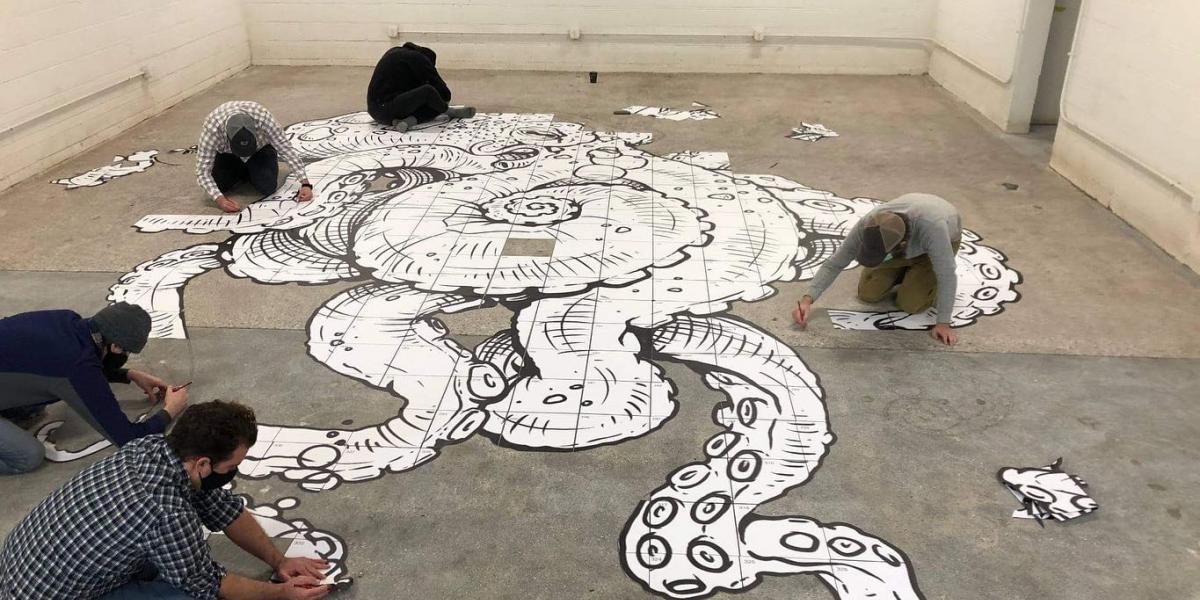 Group of masked volunteers painting an octopus mural on the concrete floor with black outlines and white interior