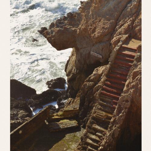 Landscape image of stone steps leading down a cliff to the seashore